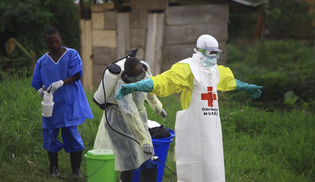 FILE - In this Sept. 9, 2018, file photo, a health worker sprays disinfectant on his colleague after working at an Ebola treatment center in Beni, Eastern Congo. Sometimes violent community resistance is complicating efforts to contain Congo‚Äôs latest Ebola outbreak, causing the rate of new cases to rise. (AP Photo/Al-hadji Kudra Maliro, File)