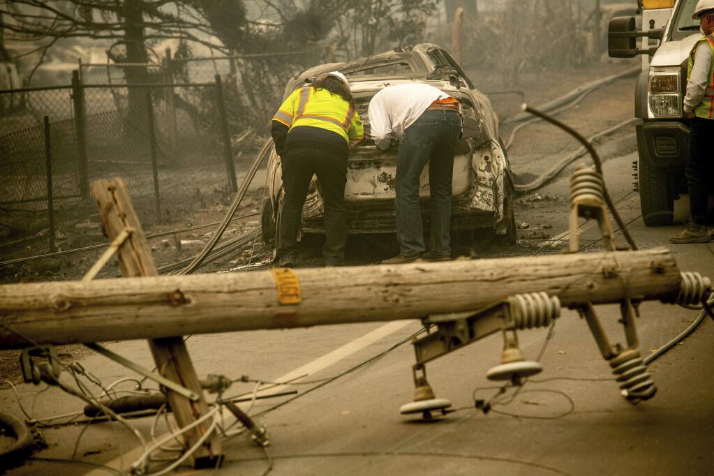 FILE - In this Nov. 10, 2018 file photo, with a downed power utility pole in the foreground, Eric England, right, searches through a friend's vehicle after the wildfire burned through Paradise, Calif. PG&E said in a new filing with the state that it determined weather conditions were no longer dangerous enough to warrant a massive power shut off on Nov. 8 - a decision that came as a massive fire was tearing through a Northern California town. (AP Photo/Noah Berger, File)