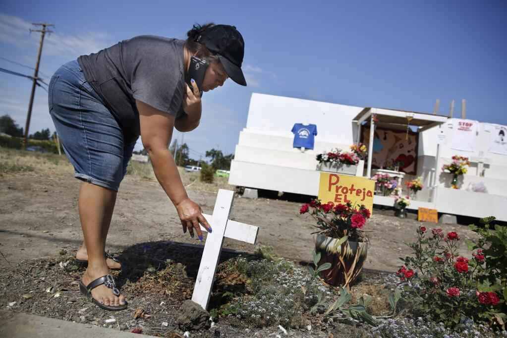 Lopez family friend Concepcion Dominguez replaces a wooden cross as she talks on the phone with Andy Lopez's mother, Sujey, and describes the vandalism at the Andy Lopez memorial site. Photo taken in Santa Rosa, on Sunday, July 19, 2015 .(BETH SCHLANKER/ The Press Democrat)