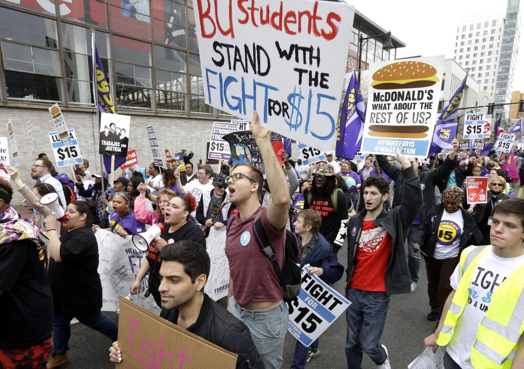 Boston University student Patrick Johnson, center, holds a sign as he joins with other protesters, including students, fast-food restaurant employees and other workers, as they march Tuesday, April 14, 2015, in Boston. Organizers of the event are calling for the nation's lowest paid workers to earn at least $15 per hour. (AP Photo/Steven Senne)
