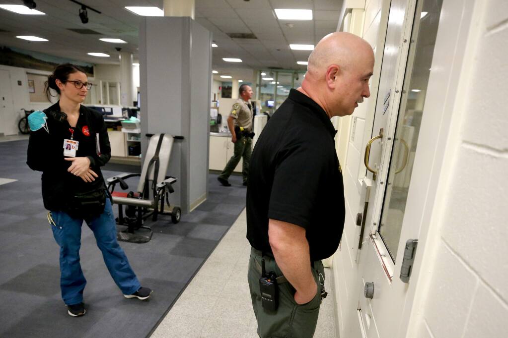 Sheriff's Office Correctional Lt. Don Huddleston and medical staff member Katie McGlothern, RN, communicate with an inmate in a negative-pressure cell about going to the hospital to be checked for COVID-19 after she developed a fever and had a potential exposure before her arrest. Photo taken in the booking area of the Sonoma County Main Adult Detention Facility in Santa Rosa on Sunday, March 15, 2020. (Beth Schlanker / The Press Democrat)