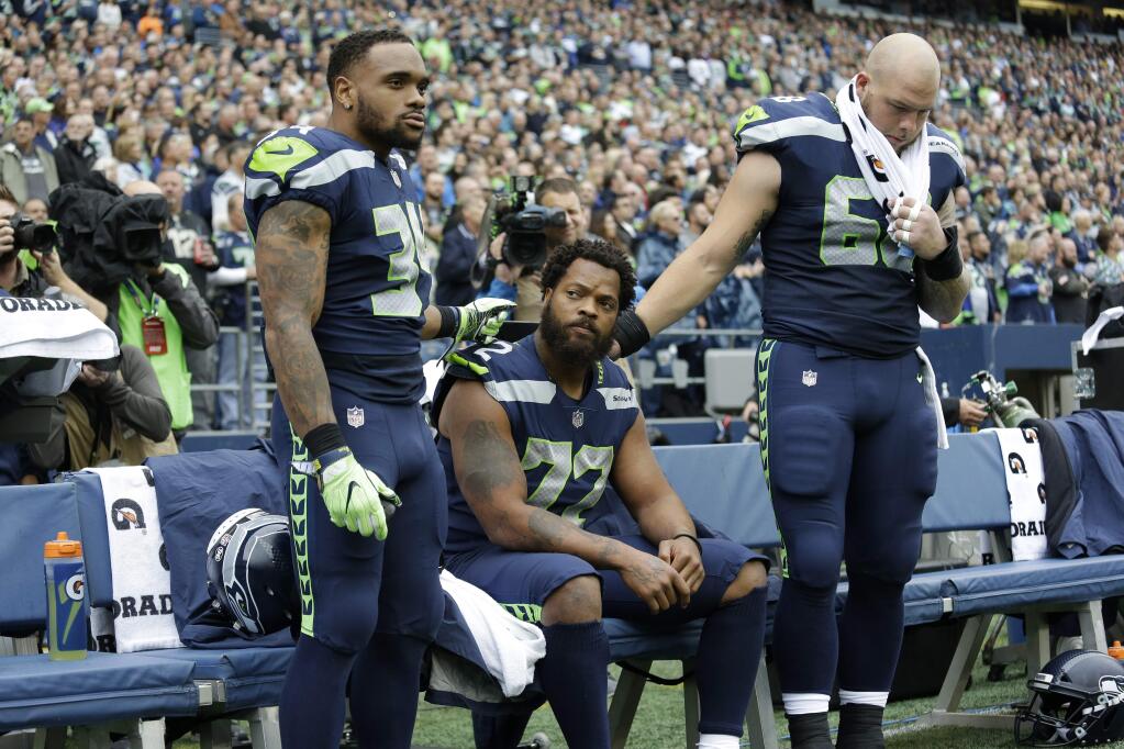 Seattle Seahawks defensive end Michael Bennett, center, is joined by teammates Thomas Rawls, left, and Justin Britt, right, as he sits during the singing of the national anthem before a game against the San Francisco 49ers, Sunday, Sept. 17, 2017, in Seattle. (AP Photo/Elaine Thompson)