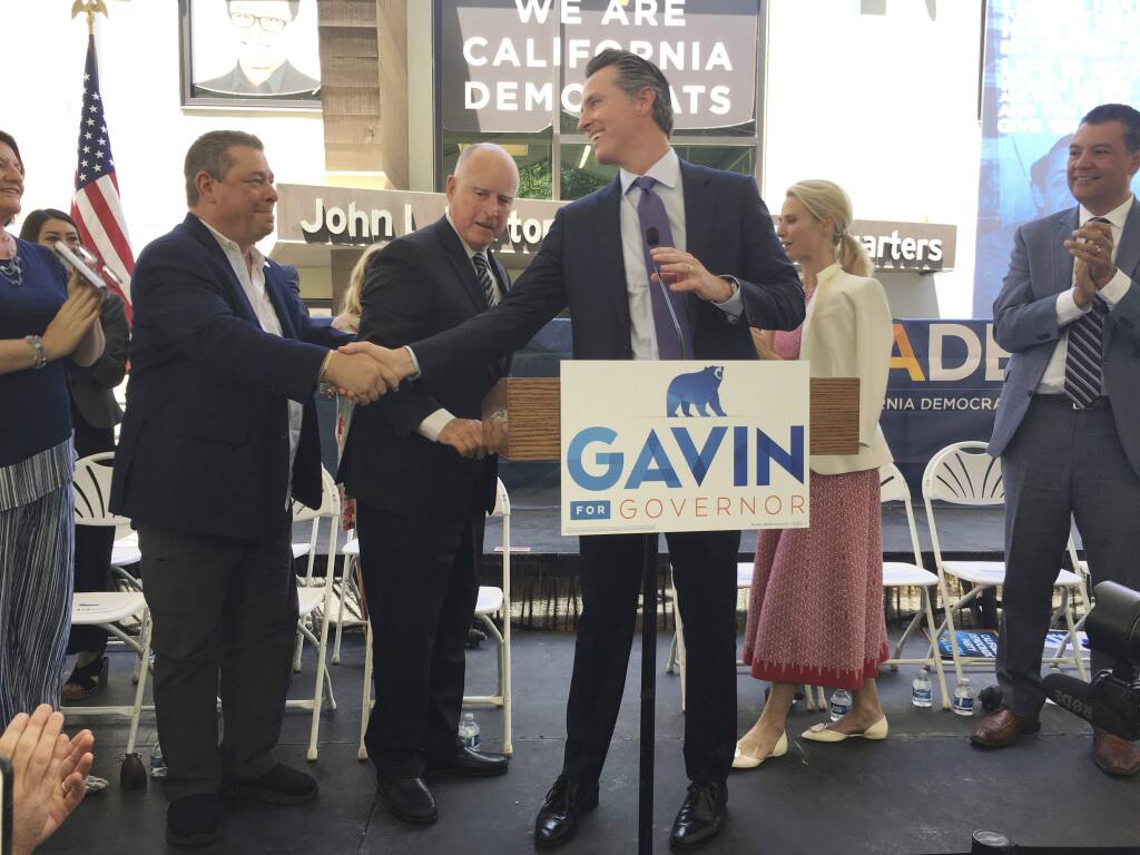 Lt. Gov. Gavin Newsom, at podium, shakes hands with California Democratic Party Chairman Eric Bauman as Gov. Jerry Brown watches during a unity rally at state Democratic headquarters in Sacramento, Calif. on Wednesday, June 13, 2018. Brown endorsed Newsom Wednesday in the race to replace him as California governor.(AP Photo/Jonathan J. Cooper)