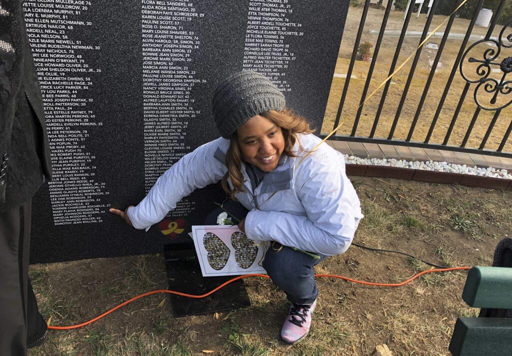 Erica Harden, of Sacramento, Calif., points out the names of six of her relatives who died in Jonestown, Guyana, on a portable memorial wall, which honors more than 300 children who were victims, as she attends a ceremony at Evergreen Cemetery in Oakland, Calif., Sunday, Nov. 18, 2018. Ceremonies at the California cemetery marked the mass murders and suicides 40 years ago of 900 Americans orchestrated by the Rev. Jim Jones at Jonestown, a jungle settlement in the South American country. (AP Photo/Tim Reiterman)