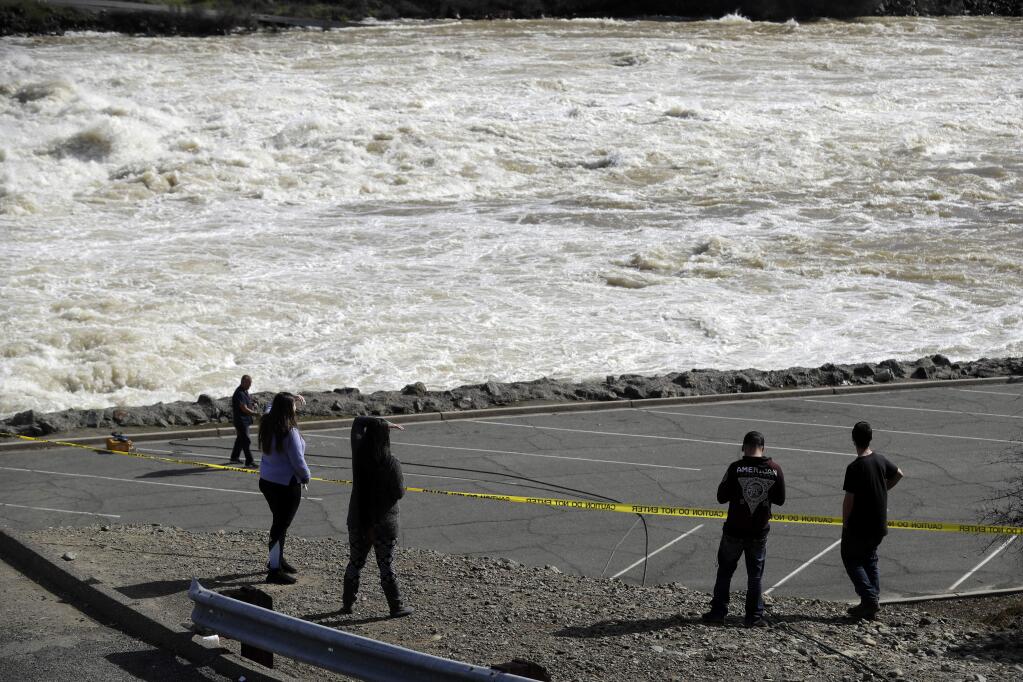 The gushing waters of the Feather River, downstream from a damaged dam, draw curious onlookers Tuesday, Feb. 14, 2017, in Oroville, Calif. Workers are rushing to repair the barrier at the nation's tallest dam after authorities on Sunday ordered the evacuation for everyone living below the lake amid concerns the spillway could fail and send water roaring downstream. (AP Photo/Marcio Jose Sanchez)