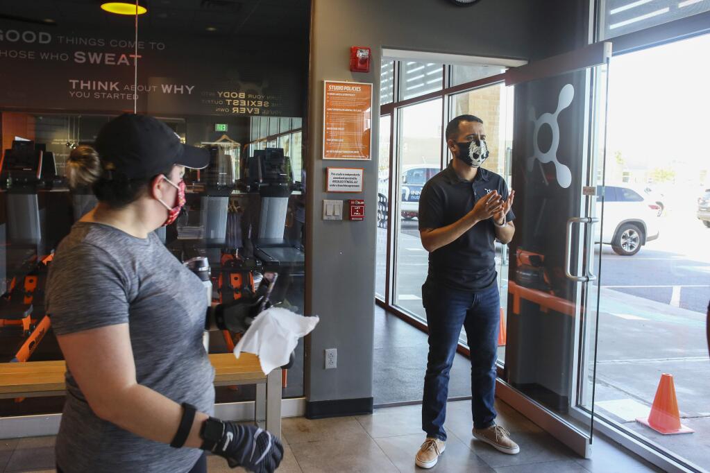 Studio manager Luis Flores says goodbye to gym users Monday, May 18, 2020, as he and his staff wait to close the gym to sanitize equipment between classes at Orangetheory Fitness in Brownsville, Texas. (Denise Cathey/The Brownsville Herald via AP)