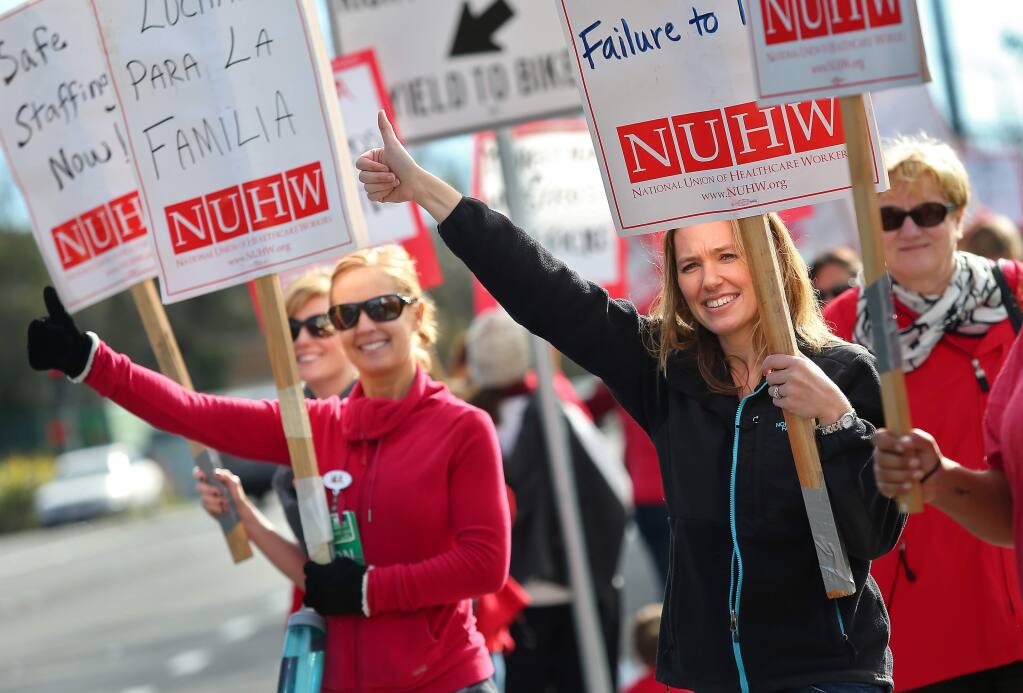 Amy Urban, right, a marriage and family therapist, and Erin Byrn, left, a registered nurse, signal to motorists along Mendocino Avenue, as they participate in a strike in front of Kaiser Permanente in Santa Rosa on Monday, January 12, 2015. Mental health professionals are striking to protest stalled contract negotiations, and what they say is insufficient staffing and patient care.(Christopher Chung/ The Press Democrat)