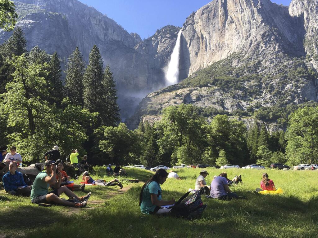 In this May 25, 2017 file photo, a class of eighth grade students and their chaperones sit in a meadow at Yosemite National Park below Yosemite Falls. The entrances to Yosemite National Park stayed open Saturday amid the partial government shutdown, but visitor centers were closed, National Park Service programs were canceled and campgrounds were not staffed. (AP Photo/Scott Smith, File)