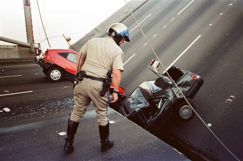 In this photo taken Oct. 17, 1989, a California Highway Patrol Officer checks the damage to cars that fell when the upper deck of the Bay Bridge collapsed onto the lower deck after the Loma Prieta earthquake in San Francisco. (AP Photo/George Nikitin)