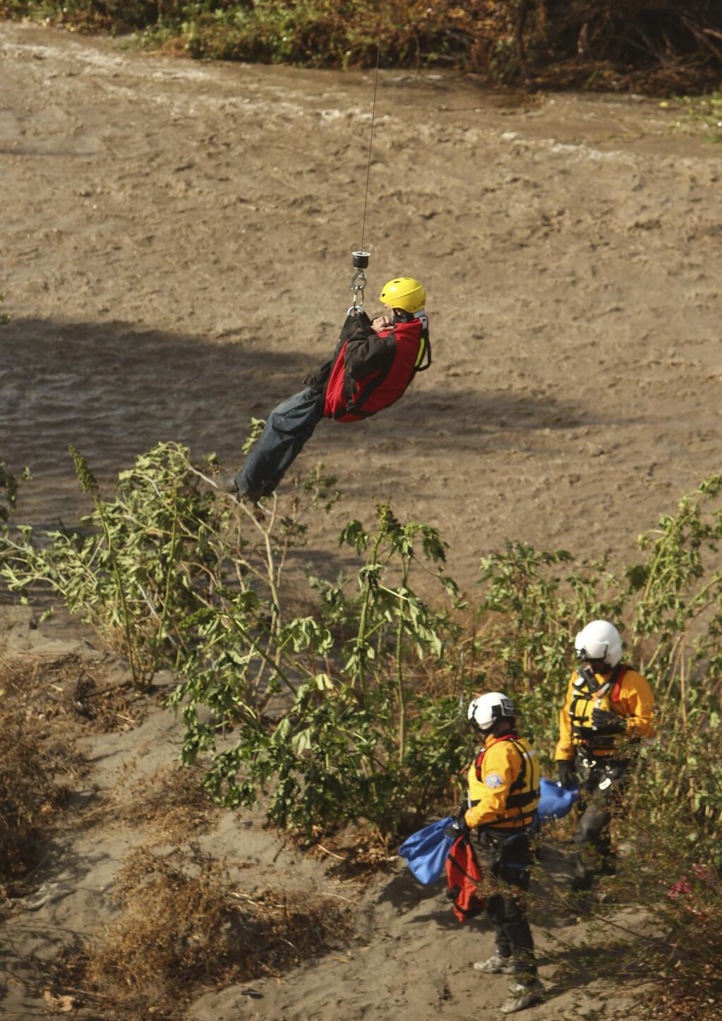 A man is hoisted out with the help of a San Bernardino County Sheriff's helicopter on Tuesday, Jan. 9, 2018, in the Santa Ana River and near the borders of Rialto, Colton, and Riverside, Calif. Three people and a dog were rescued by a helicopter after large amounts of rain fell, trapping the group at a homeless encampment in the river. (Stan Lim/Los Angeles Daily News via AP)