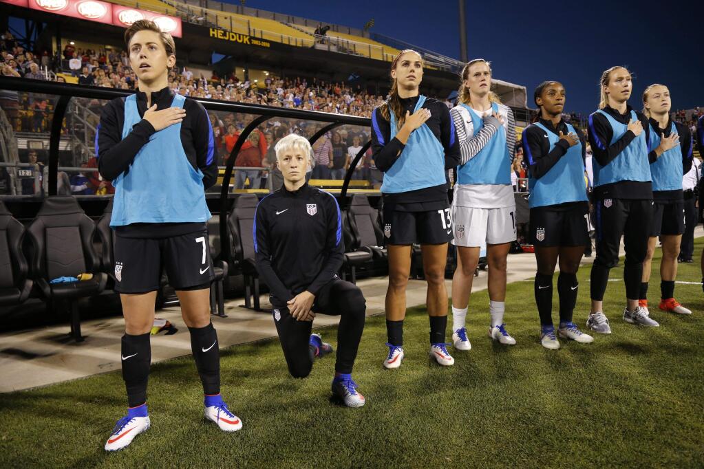 United States' Megan Rapinoe, second from left, kneels during the playing of the national anthem before the soccer match against Thailand, Thursday, Sept. 15, 2016 in Columbus, Ohio. Rapinoe did not start the game against Thailand at Mapfre stadium. She knelt from a spot near the bench while the fellow reserves around her stood. (Kyle Robertson/The Columbus Dispatch via AP)