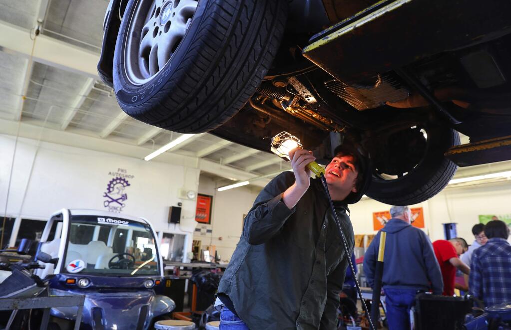 Jake Perinoni looks at the undercarriage of his sisters vehicle, after raising it on a lift during his automotive technology class at Petaluma High School, on Thursday, April 19, 2018. (Christopher Chung/ The Press Democrat)
