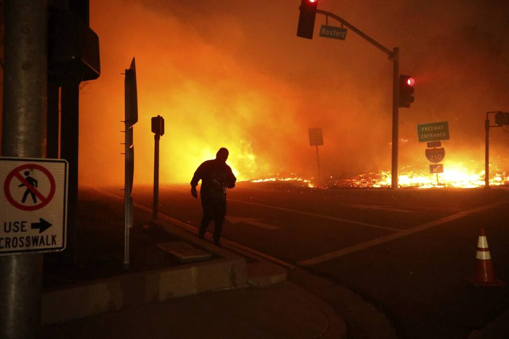 FILE - In this Friday, Oct. 11, 2019 file photo, a bystander watches the Saddleridge fire in Sylmar, Calif. California's largest utility Pacific Gas & Electric Corp pledged to improve communications but reminded state regulators that its 'difficult decision' to pre-emptively shut off power to more than 2 million people last week may have prevented deadly wildfires. (AP Photo/David Swanson, File)