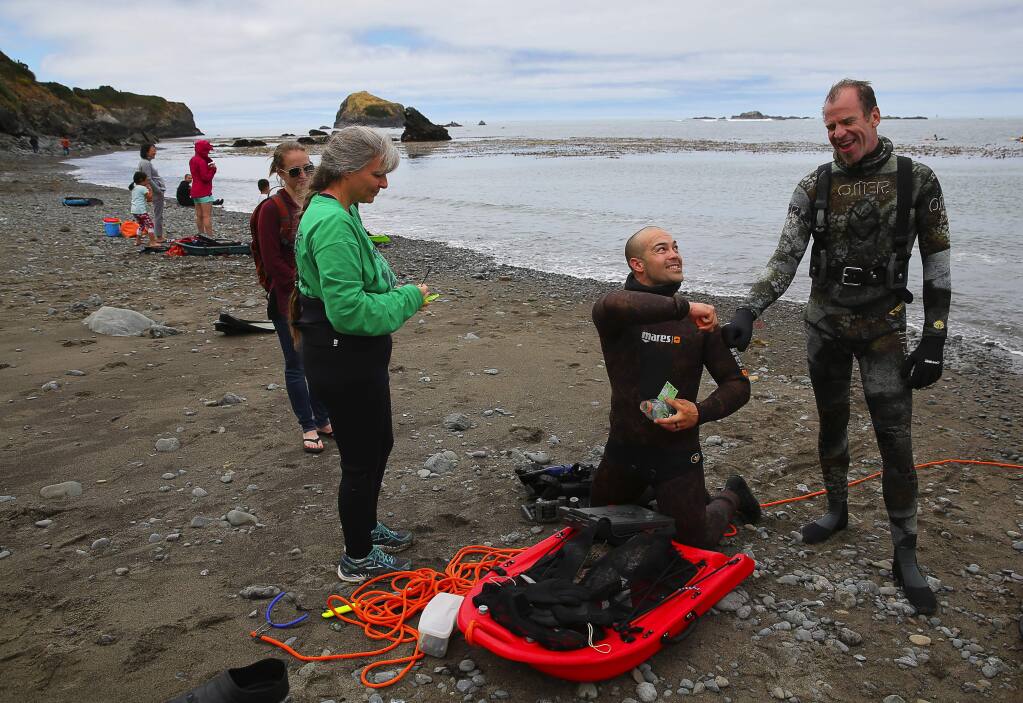 Billy Brown, center, gets a fist bump from his abalone dive instructor and guide Keith Peschel, right, while guide Leslie Russo walks him through properly tagging his abalone at Van Damme State Beach, in Little River on Monday, June 26, 2017. (Christopher Chung/ The Press Democrat)
