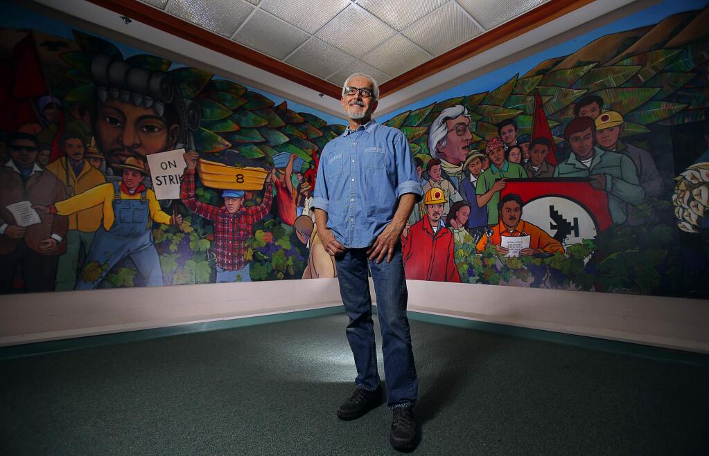 Artist Mario Uribe at Elsie Allen High School, standing in front of a mural he created with students over the course of seven years. Uribe's latest plan for a purposeful art piece will shine a light on the homeless in Roseland that will reveal their lives, hopes and fears. (Christopher Chung/ The Press Democrat)