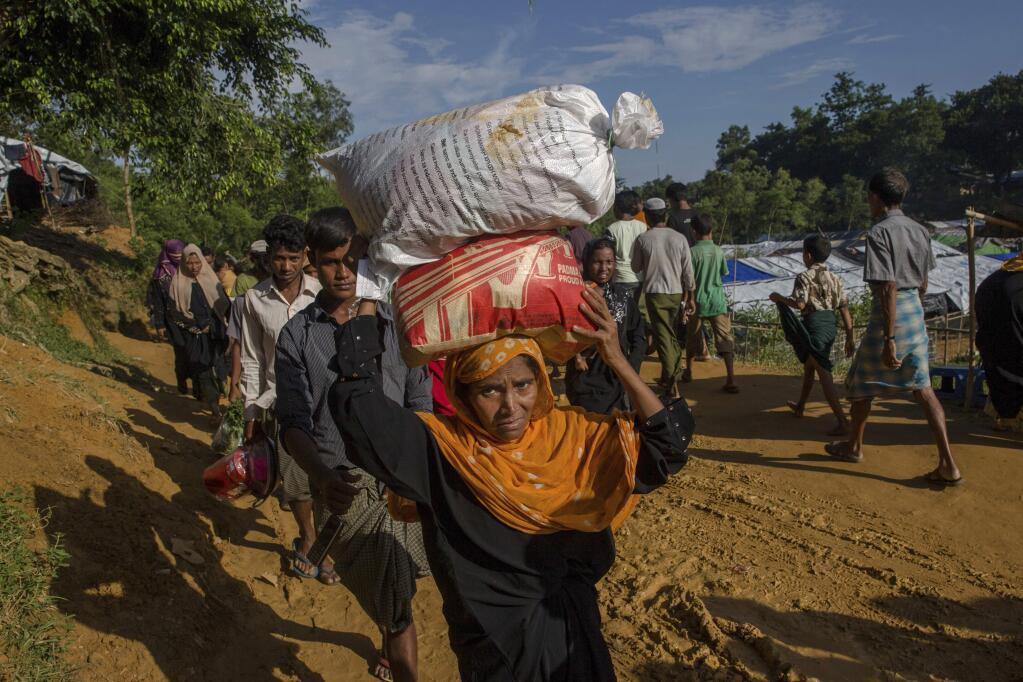 A Rohingya Muslim woman, who crossed over from Myanmar into Bangladesh, walks back to her shelter after collecting handouts at Kutupalong refugee camp, Bangladesh, Thursday, Sept. 21, 2017. With Rohingya refugees still flooding across the border from Myanmar, those packed into camps and makeshift settlements in Bangladesh are desperate for scant basic resources and fights erupt over food and water. (AP Photo/Dar Yasin)