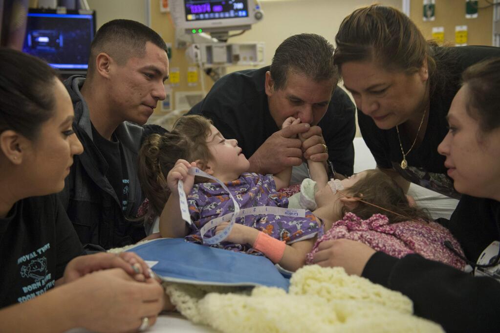 In this photo taken Tuesday, Dec. 6, 2016, the family of conjoined twins Erika and Eva Sandoval, left to right, Aniza, Emilio, Art, Aida and Esmeralda, surround them in the pre-operating room the morning of their separation surgery in Palo Alto, Calif. Eva and Erika Sandoval have become two separate toddlers following a 17-hour marathon surgery at the Lucile Packard Children's Hospital Stanford that began on Tuesday, officials said. The 2-year-old Sacramento area girls were born conjoined from the chest down and shared a bladder, liver, parts of their digestive system and a third leg. (Lezlie Sterling/The Sacramento Bee via AP)