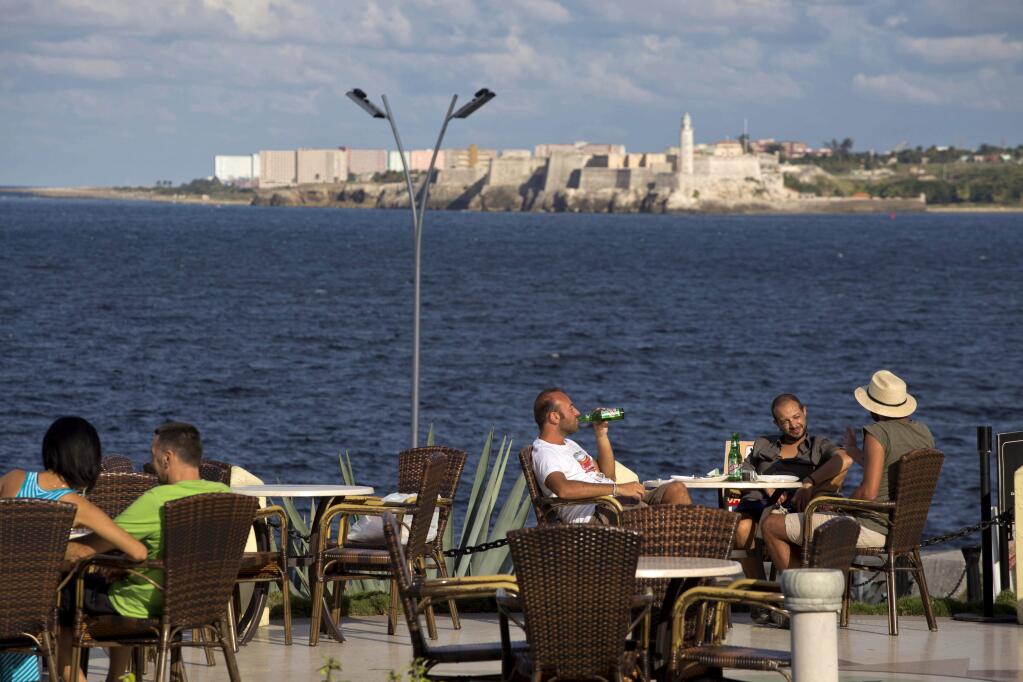 Tourists take a few beers at the Hotel National, with view of Morro Castle behind them in Havana, Cuba, Wednesday, Dec. 17, 2014. After a half-century of Cold War acrimony, the United States and Cuba abruptly moved on Wednesday to restore diplomatic relations _ a historic shift that could revitalize the flow of money and people across the narrow waters that separate the two nations. The U.S. is easing restrictions on travel to Cuba, including for family visits, official government business and educational activities. But tourist travel remains banned. (AP Photo/Desmond Boylan)