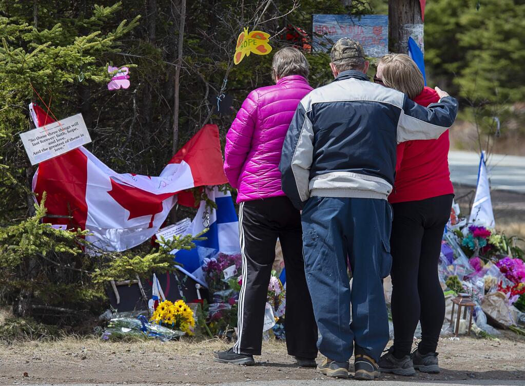 A family pays their respects to victims of the mass killings at a checkpoint on Portapique Road in Portapique, Nova Scotia, on Friday, April 24, 2020. At least 22 people are dead after a man, who at one point wore a police uniform and drove a mock-up cruiser, went on a murder rampage in Portapique and several other Nova Scotia communities. (Andrew Vaughan/The Canadian Press via AP)