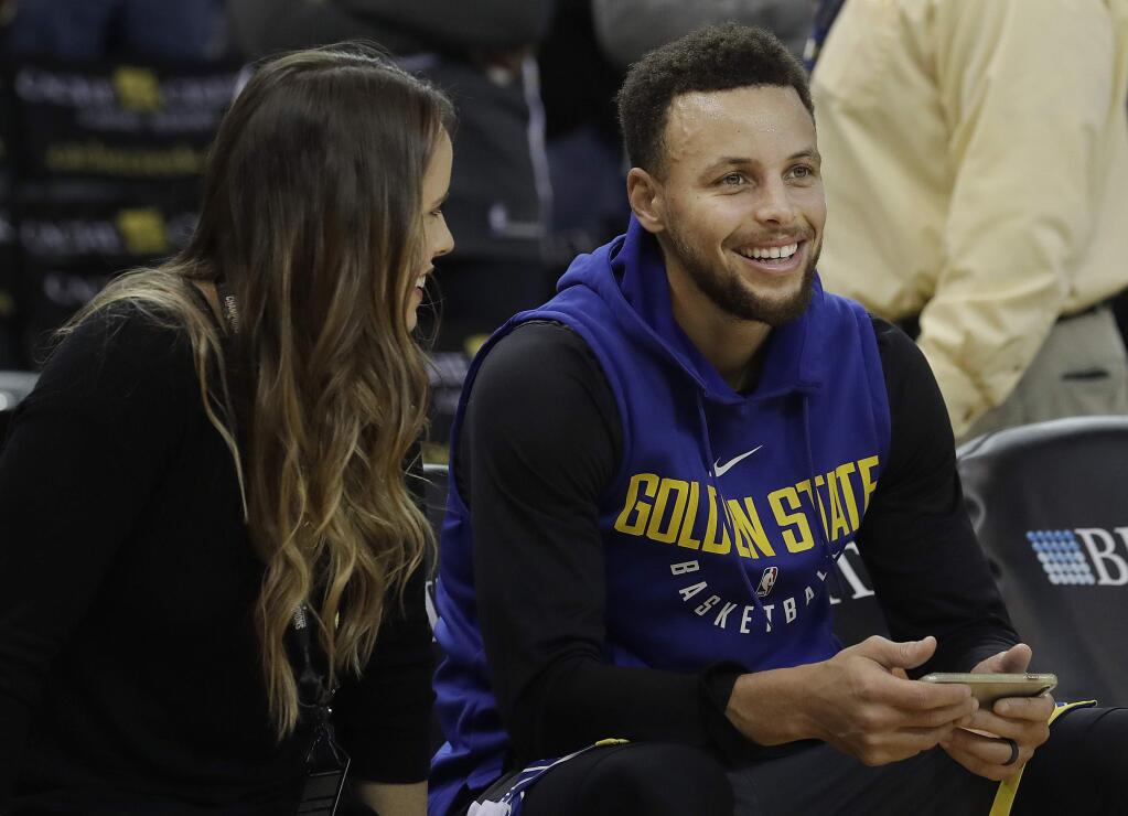 Golden State Warriors guard Stephen Curry, right, smiles as he talks with the team's director of corporate communications, Lisa Goodwin, before a game against the Denver Nuggets in Oakland, Saturday, Dec. 23, 2017. (AP Photo/Jeff Chiu)