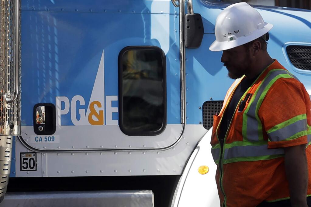 FILE - In this Aug. 15, 2019, file photo, a Pacific Gas & Electric worker walks in front of a truck in San Francisco. Pacific Gas & Electric's complex plan for emerging from bankruptcy may face a make or break moment during a court hearing Tuesday, April 7, 2020, that will re-examine the merits of a $13.5 billion settlement with the victims of catastrophic wildfires caused by the utility. (AP Photo/Jeff Chiu, File)