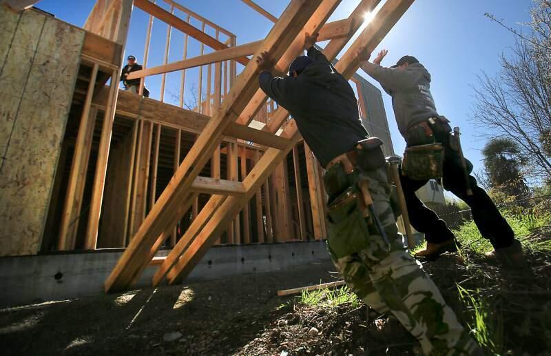 Miguel Gonzalez, left, and Raul Rivas combine efforts to lift the framing of an exterior wall as Raul Magana, top left, pulls the structure toward the house in March, as the three build a granny unit in Santa Rosa. (Kent Porter/The Press Democrat)