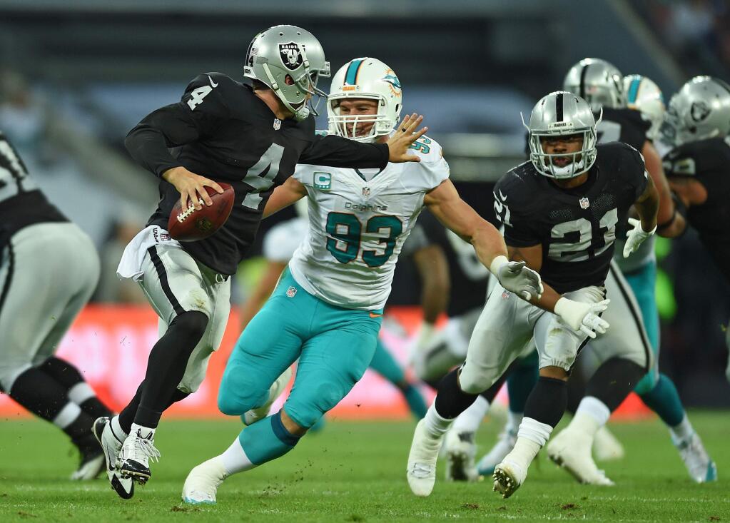 Oakland Raiders' Derek Carr, left, tries to fend off Miami Dolphins' Jason Trusnik during the NFL football game at Wembley Stadium in London, Sunday, Sept. 28, 2014. (AP Photo/Tim Ireland)