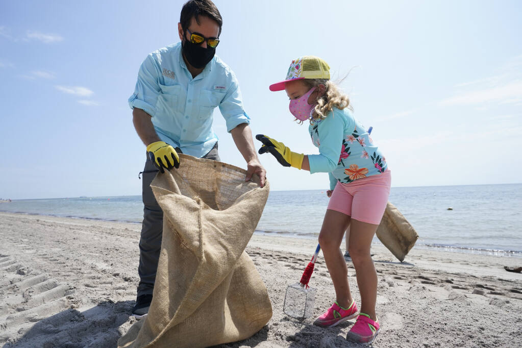 Ed Prichard, left, site manager for the Miami EcoAdventures unit at Crandon Park and Charlotte Gonzalez, 7, pick up trash and micro-plastics while taking part in an Earth Day beach cleanup, Thursday, April 22, 2021, at Crandon Park in Key Biscayne, Fla. (AP Photo/Wilfredo Lee)