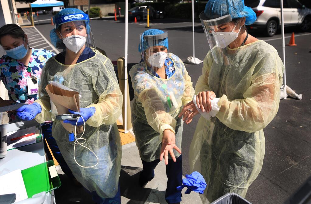 From left, Sayde Galindo, Judith Placencia, Evelyn Gomez  and Paula Pelavin decontaminate after obtaining a swab sample during drive up COVID-19 testing at Petaluma Health Center, Tuesday, July 14, 2020.   (Kent Porter / The Press Democrat) 2020