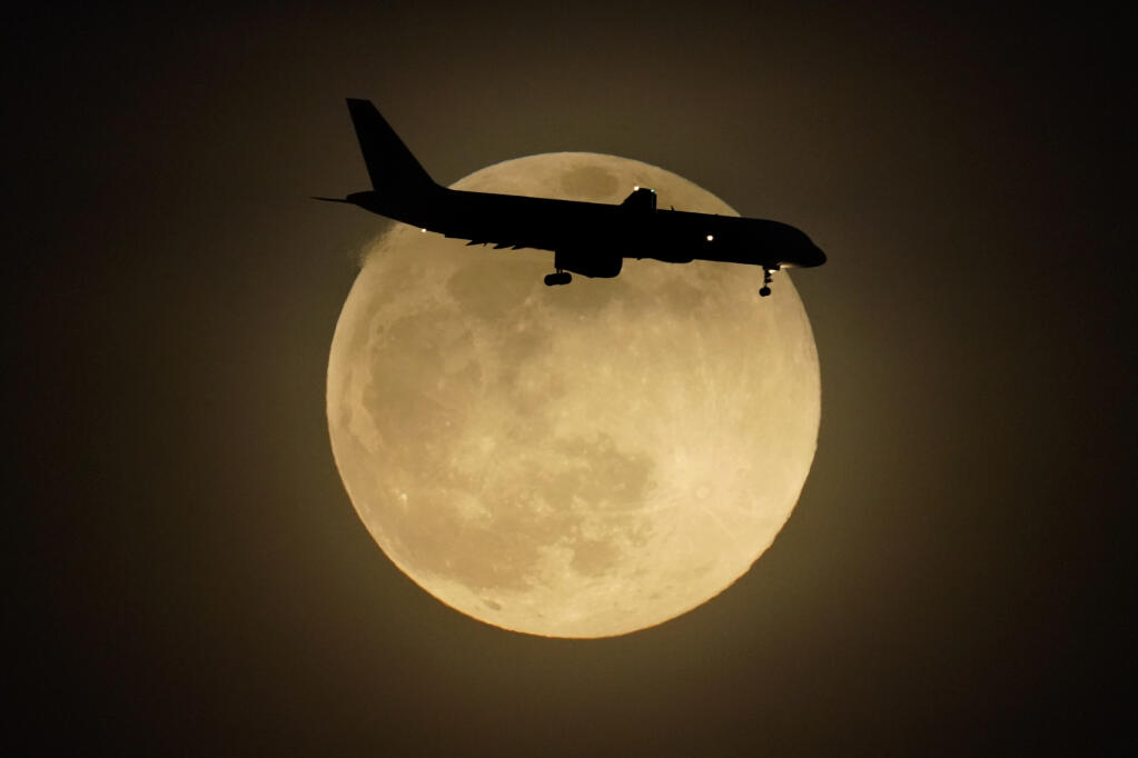 A jet is silhouetted by the rising moon as it approaches Louisville International Airport, Monday, April 26, 2021, in Louisville, Ky. This moon is a supermoon, meaning it appears larger than an average full moon because it is nearer the closest point of its orbit to Earth. (AP Photo/Charlie Riedel)