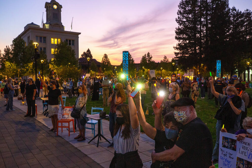 Susan Bercu, lower right, of Santa Rosa embraces her husband Ken Smith raise their smartphone lights with Bercu's granddaughter Charlotte Papes, 14, of Richmond, as others hold up their candles during a vigil to honor the memory of Supreme Court Justice Ruth Bader Ginsburg at Old Courthouse Square in Santa Rosa, California, on Saturday, September 19, 2020. (Alvin A.H. Jornada / The Press Democrat)
