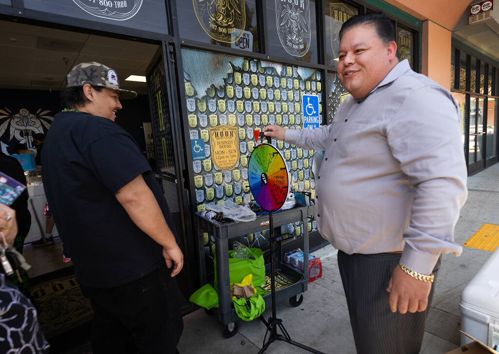 Santa Rosa city councilman Eddie Alvarez, right, was still smiling as he encouraged a line of customers to spin the wheel on 4/20 at The Hook cannabis dispensary in Santa Rosa Thursday, April 20, 2023. Owner Alvarez stated he will comply with a Santa Rosa city cease and desist order to close amid a permit and tax dispute. (John Burgess/The Press Democrat)