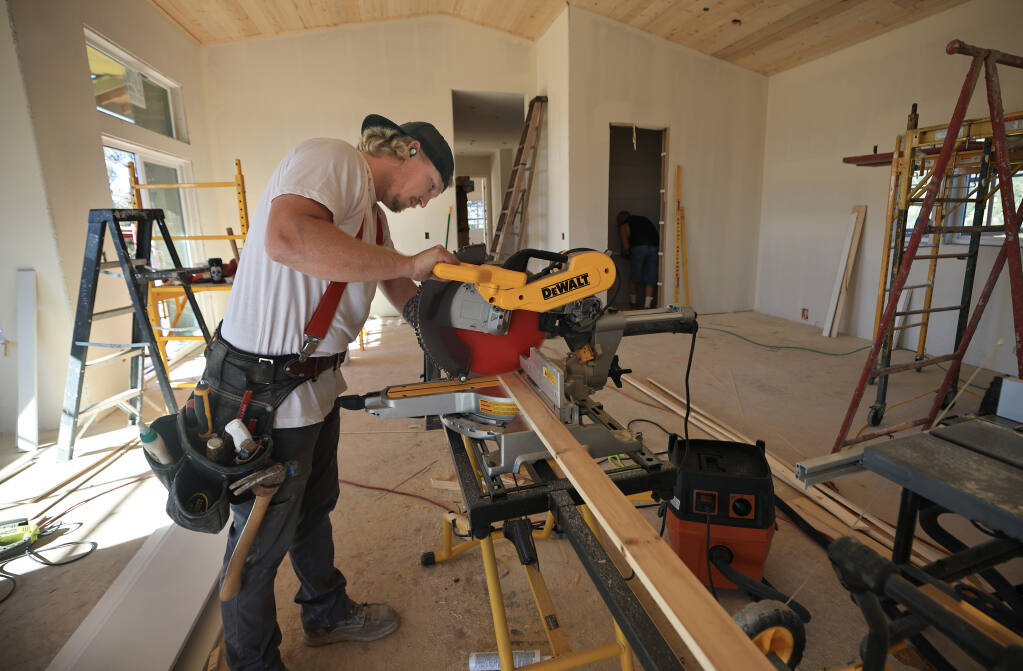 Cody McPheron, left, a carpenter with Wright Builders, cuts to size ceiling trim for a Tubbs fire home rebuild, Thursday, Nov. 11, 2021.  At right is fellow carpenter Uriah Wilder, installing shelving in a kitchen pantry.  (Kent Porter / The Press Democrat) 2021