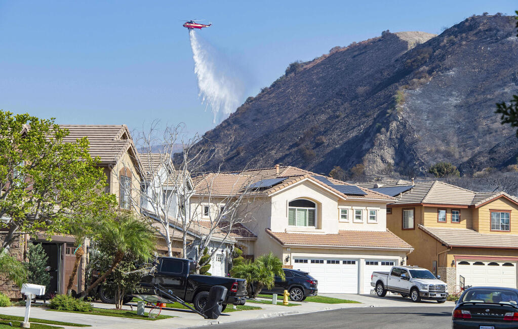 A helicopter drops water onto hot spots of the Silverado Fire behind homes in the Foothill Ranch area near  Lake Forest, Calif., Wednesday, Oct. 28, 2020. (Mark Rightmire/The Orange County Register via AP)