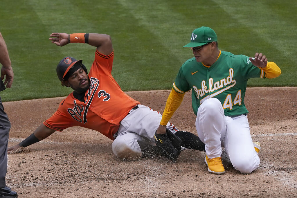The Baltimore Orioles’ Maikel Franco, left, slides home to score against Oakland Athletics pitcher Jesus Luzardo during the third inning in Oakland on Saturday, May 1, 2021. (Jeff Chiu / ASSOCIATED PRESS)