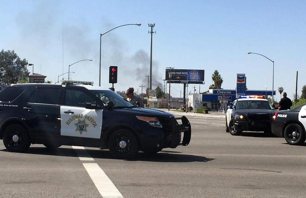 Highway patrol officers block off Herndon Avenue at Highway 99 where smoke can be seen at the fire from a gas line rupture in northwest Fresno. A large gas explosion closed both directions of a major highway in Central California and injured at least 11 people, three of them critically, authorities said Friday, April 17, 2015. (Hannah Furfaro/The Fresno Bee via AP)