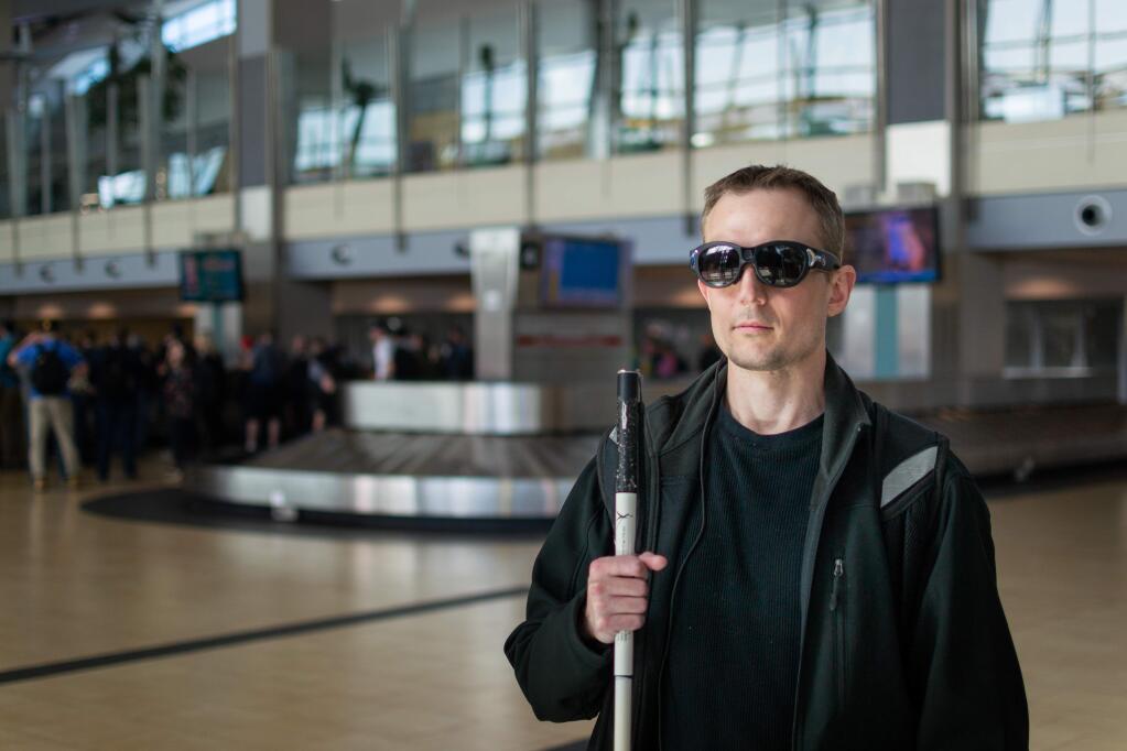 An Aira user, wearing Horizon Smart Glasses and holding a white cane, uses Aira for a description at an airport with the baggage claim area in the background. (AIRA)