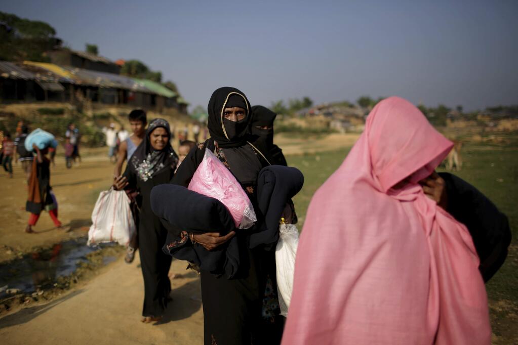 FILE - In this Tuesday, Nov. 21, 2017, file photo, Rohingya Muslim women carry blankets and other supplies they collected from aid distribution centers in Kutupalong refugee camp in Bangladesh. The United States declared the ongoing violence against Rohingya Muslims in Myanmar to be 'ethnic cleansing' on Wednesday, Nov. 22, putting more pressure on the country's military to halt a brutal crackdown that has sent more than 600,000 refugees flooding over the border to Bangladesh. (AP Photo/Wong Maye-E, File)