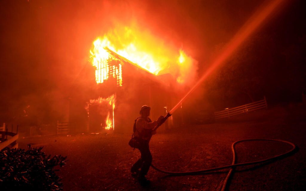 A Downey firefighter concentrates on wetting down a house adjacent to a burning barn, Sunday Oct. 27, 2019, as the Kincade fire pushed down to Shiloh Ridge and  Faught Road east of Windsor.  (Kent Porter/The Press Democrat, 2019)