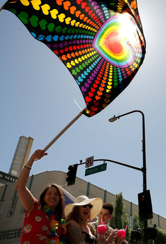 Megan Dwyer, left, waves a flag while riding with Kortney McMillen and Steven Basurto during the Sonoma County Pride Parade in Santa Rosa, California, on Saturday, June 1, 2019. (Alvin Jornada / The Press Democrat)
