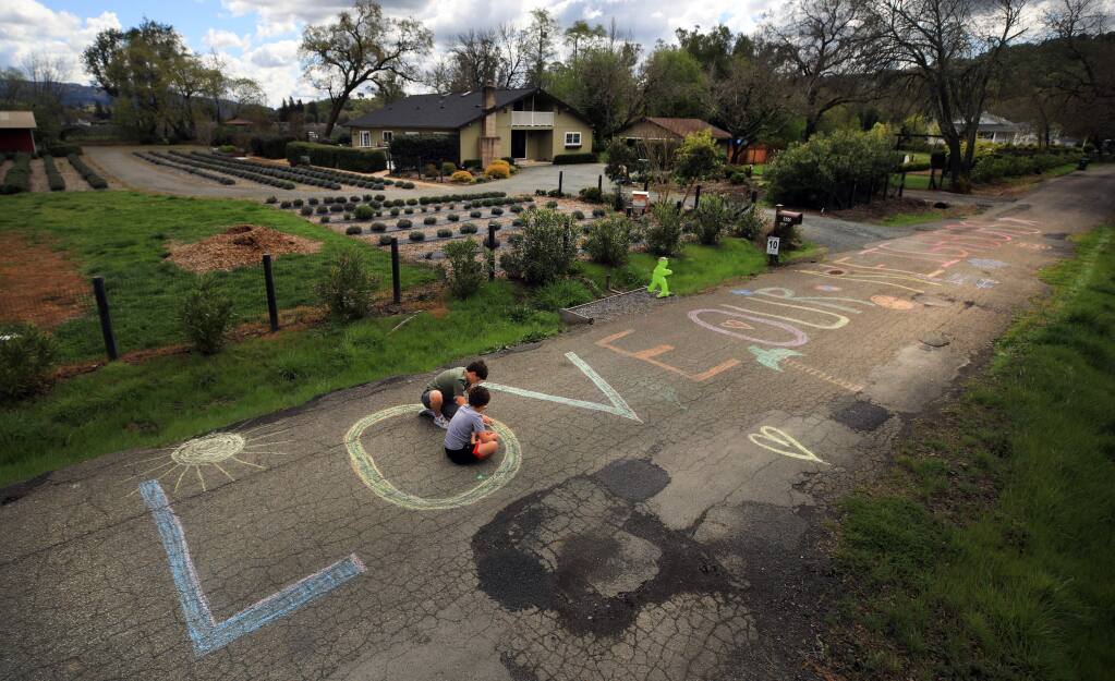 Jayden and Josh Stocks of Kenwood put the finishing touches on a large street chalk message that says 'We love our neighbors.' The art is part of their art class from online schooling on Thursday, March 26, 2020. (Kent Porter / The Press Democrat) 2020