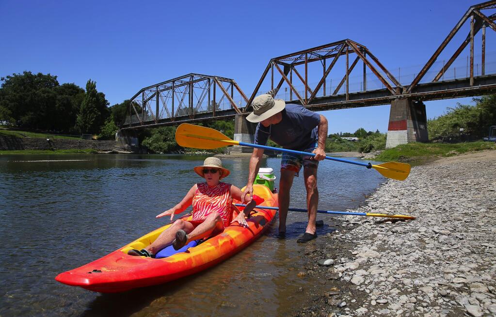 Steve McCarthy helps his wife, Trish, out of their kayak as they return to River's Edge Kayak & Canoe, at Healdsburg Veterans Memorial Beach on Monday, May 22, 2017. (Christopher Chung/ The Press Democrat)