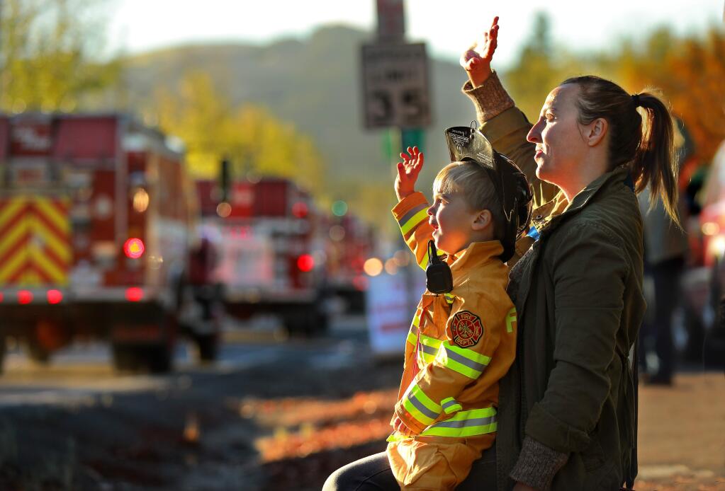 Jack, 3, and Katie Bozin wave to fire trucks returning to encampments at the Sonoma County Fairgrounds after a night on the fire lines early Saturday morning. More than 200 people gathered along Brookwood Ave. in Santa Rosa to give their thanks to first responders. (photo by John Burgess/The Press Democrat)