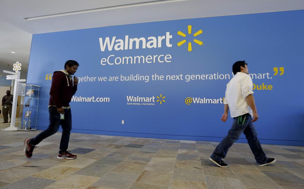 FILE - In this Wednesday, Sept. 18, 2013, file photo, two Wal-Mart employees walk past a sign in the lobby at the Walmart.com office in San Bruno, Calif. Wal-Mart's acquisition of Jet.com is accelerating its progress in e-commerce as it works to narrow the gap between itself and online leader Amazon. Wal-Mart is betting its online future on essentials like produce and groceries and has adjusted its shipping strategy. But Amazon keeps innovating too. (AP Photo/Jeff Chiu, File)