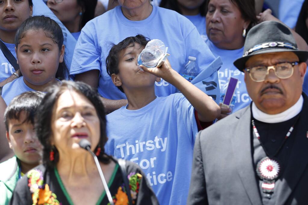 In this June 10, 2019 file photo a young man sips some water as civil rights activist Dolores Huerta, left, speaks in support of a clean water measure before the legislature, during a rally in Sacramento, Calif. Gov. Gavin Newsom signed a law Wednesday, July 24, 2019, that will redirect up to $130 million of state money meant to clean up the air to instead clean up the drinking water for more than 1 million Californians who don't have clean drinking water. (AP Photo/Rich Pedroncelli, File)