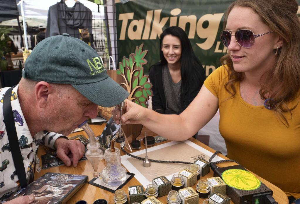 FILE - In this Thursday, June 20, 2019 file photo a Mark 'Wiz' Schulze, left, takes a puff of a cannabis concentrate from Talking Trees farm during a business to business networking event. California's legal pot market is growing, just not as fast as once expected. The state pulled in $74 million in cannabis excise taxes between April and June, after the Newsom administration in May sharply scaled back projected tax dollars from the shaky legal market. The figure released Thursday, Aug. 22, 2019, marked an increase from the first quarter, when excise tax collections hit $61 million. (AP Photo/Richard Vogel,File)