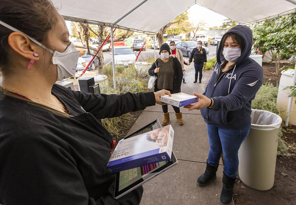 Santa Rosa Community Health Center, Lombardi campus receptionist Monica Hernandez hands out COVID test kits to Raquel Lopez and other clients waiting in line on Friday, Jan. 14, 2021. (John Burgess/The Press Democrat)