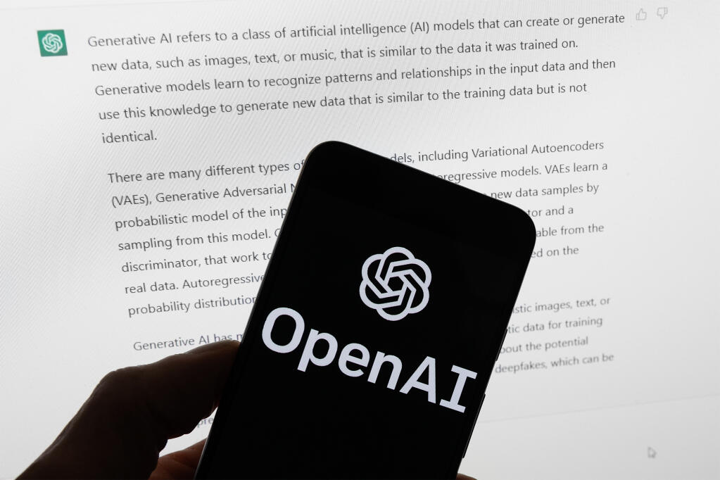 The OpenAI logo on a mobile phone in front of a computer screen displaying output from ChatGPT, on March 21, 2023. Photo by Michael Dwyer, AP Photo