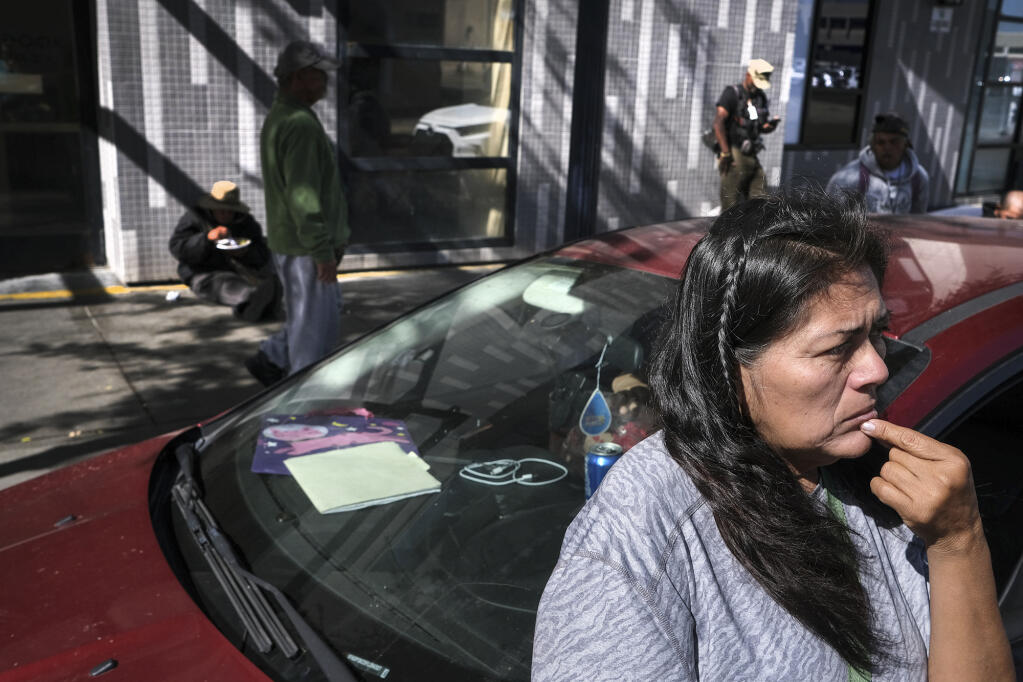 Angela Reyes Melo, 56, waits outside her car before driving to pick up supplies at a food bank on October 28, 2022, in San Diego. Reyes has been living with her son in a loaned car for the past four months. Photo by David Maung for CalMatters