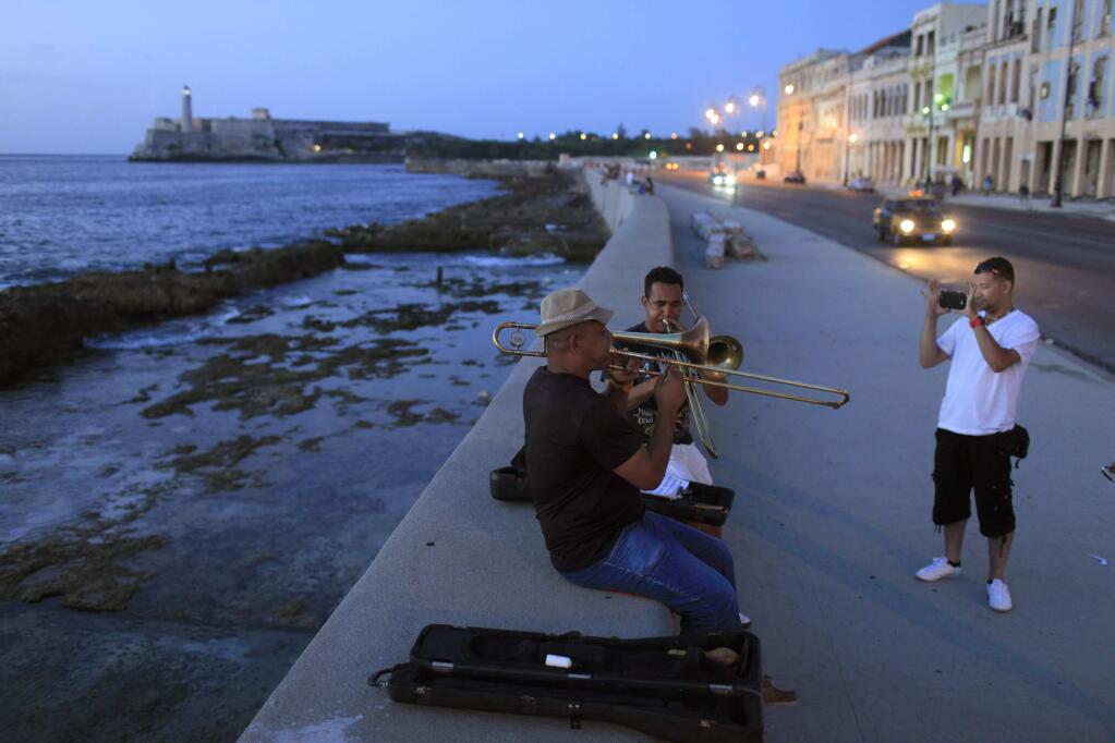 FILE - In this July 8, 2013 photo, musicians play trombones as a tourist from Colombia takes their picture along the Malecon in Havana, Cuba. President Barack Obamas announcement Wednesday, Dec. 17, 2014, of plans to re-establish diplomatic ties with the Caribbean nation gives hope to airlines, hotel chains and cruise companies _ all which have been quietly eyeing a removal of the travel ban _ that they soon will be able to bring tourists to Cuba. (AP Photo/Franklin Reyes, File)
